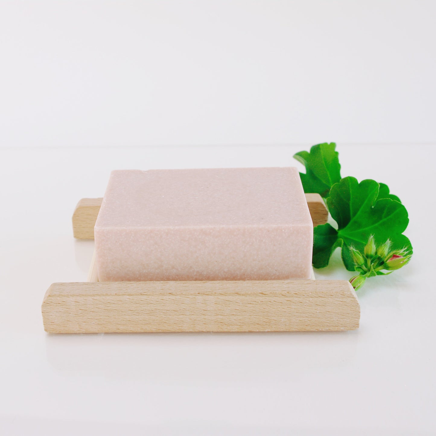 A bar of soap on wooden stand with a green leaf on a white background