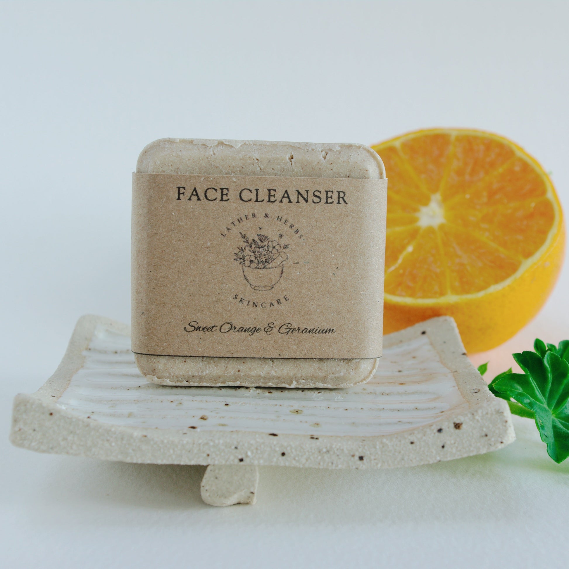 Brown facial cleansing bar on a handmade soap dish made of ceramic and an orange slice
