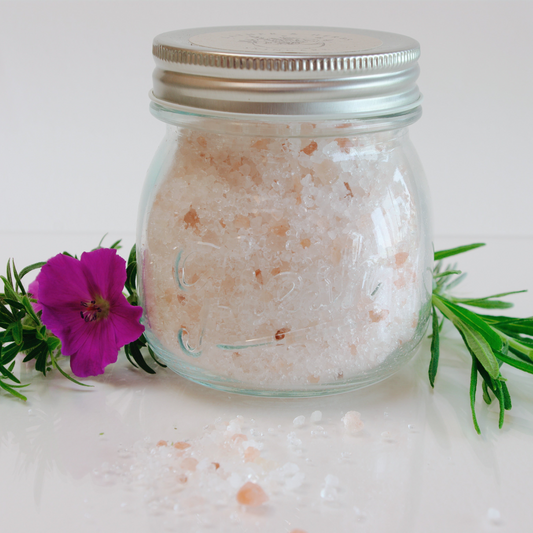 Glass jar of bath salts with a pink flower and green leaves on a white background