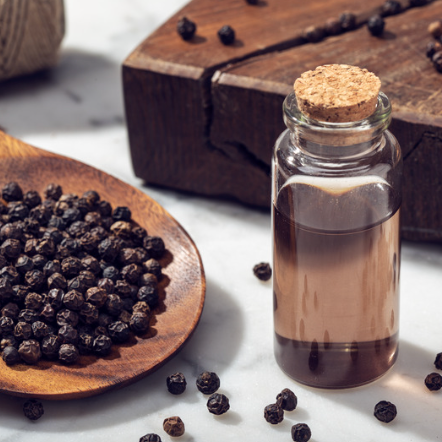 Bottle of black pepper oil with black peppercorns on a wooden board and surface.