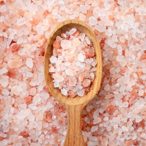 Wooden spoon filled with pink Himalayan salt crystals on a bed of pink salt.