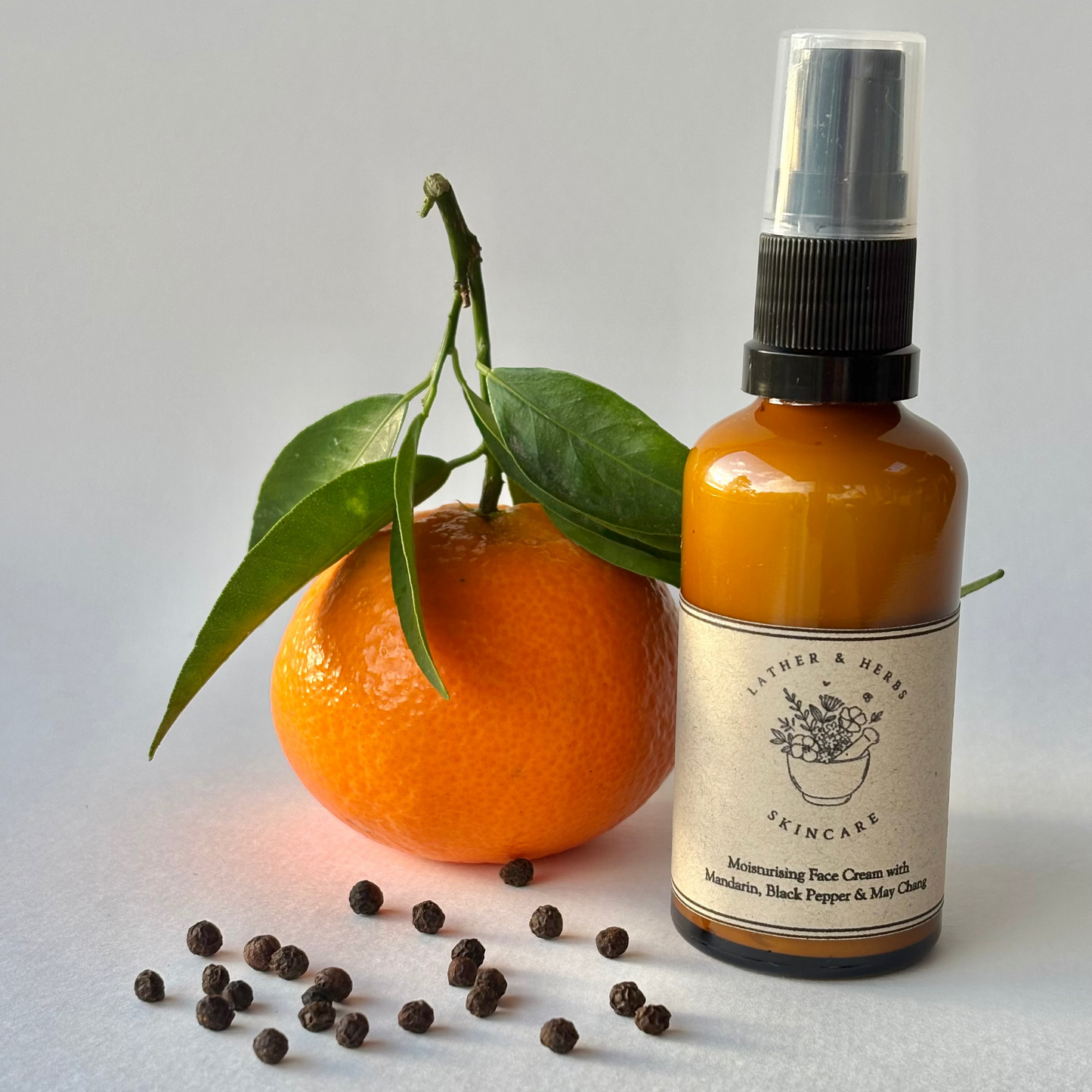 Mandarin, Black Pepper & May Chang face cream pump bottle with a mandarin and peppercorns.