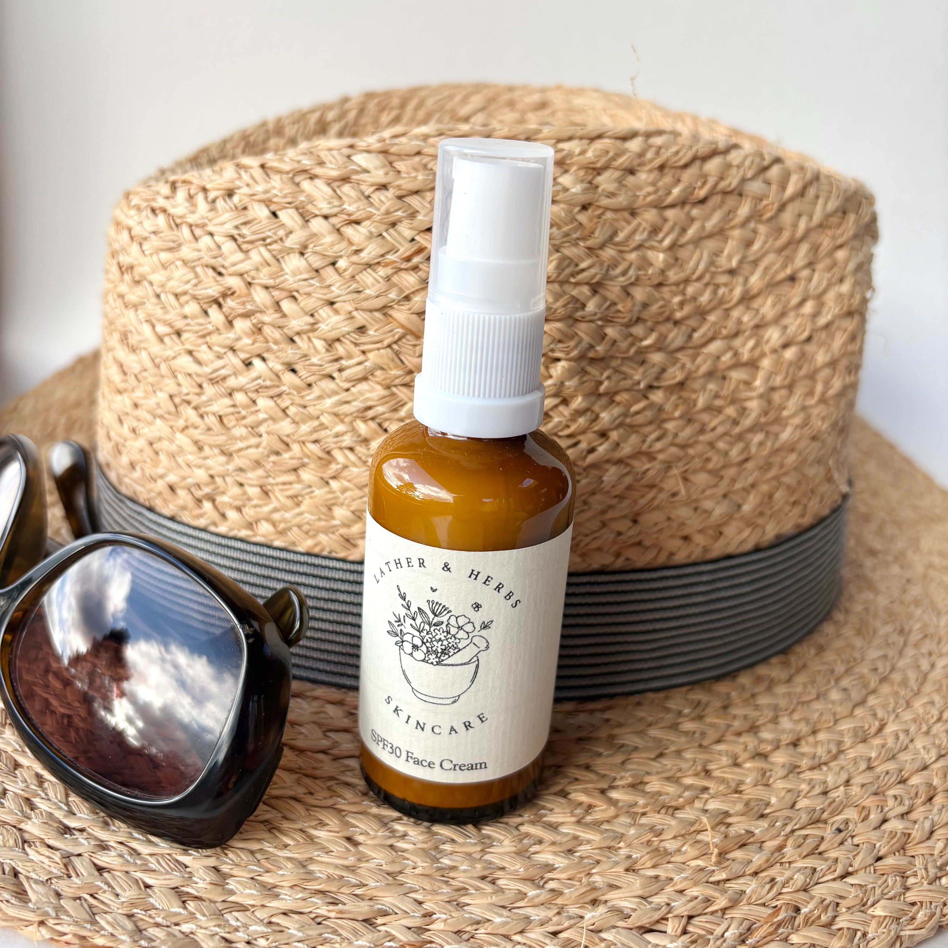 Bottle of face cream with a label, sunglasses, and a straw hat on a white background