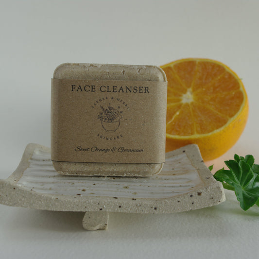 gentle face cleanser on a ceramic handmade soap dish with foliage and an orange slice